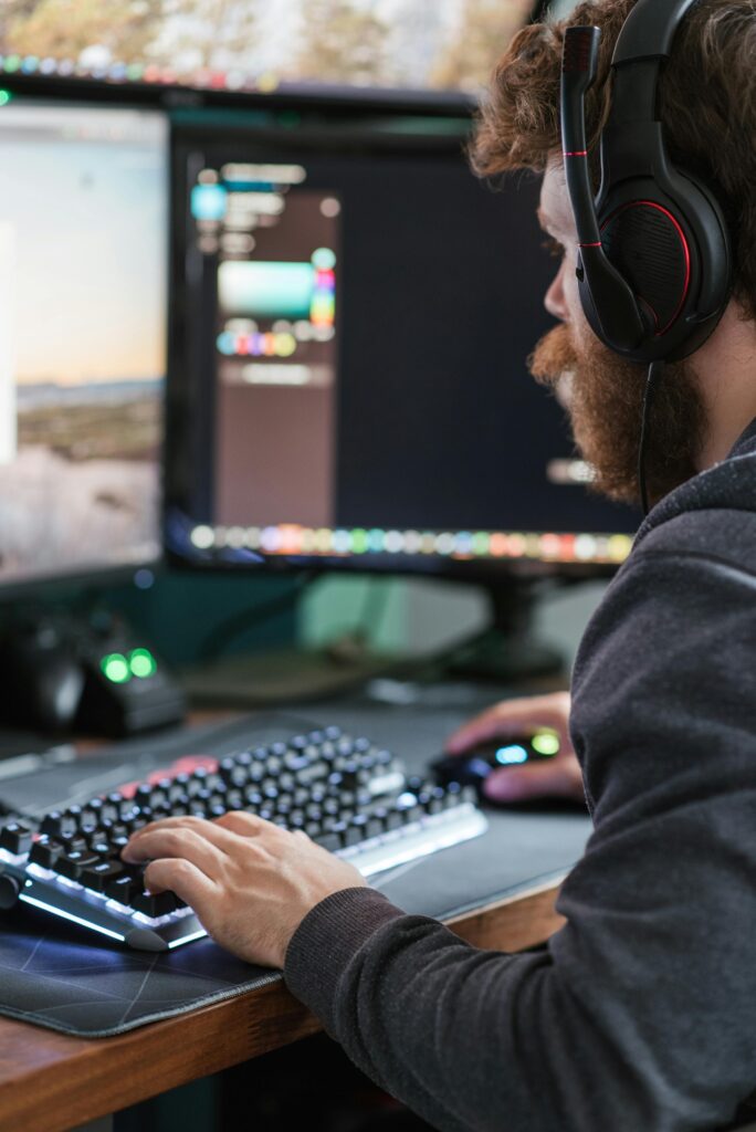 Side view crop focused bearded male wearing headset browsing modern computer while typing on keyboard
